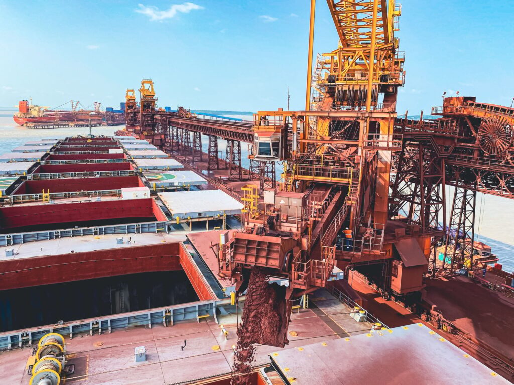 Iron ore conveyor loading cargo in the bulk carrier with a cloudy blue sky in the background