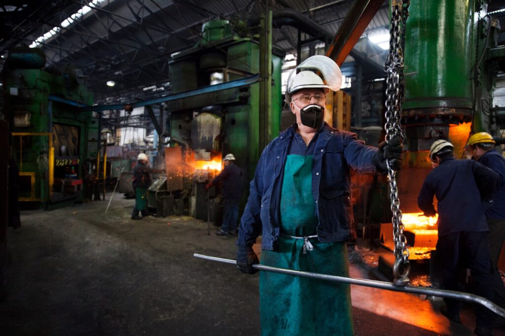 Operative prepares to hook steel billet out of furnace. Team in background using counterblow hammer