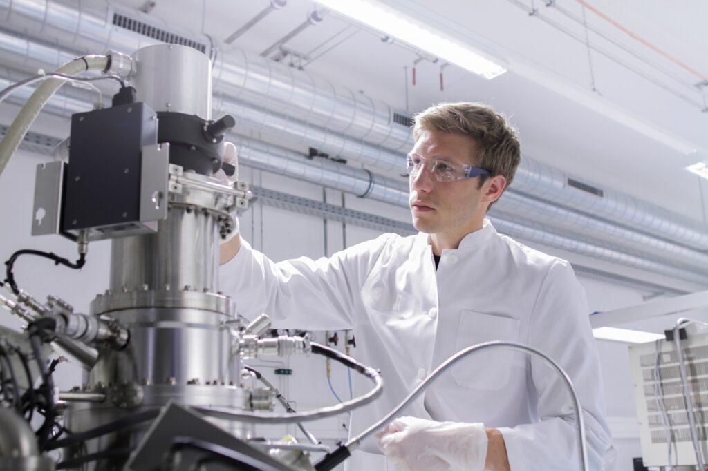 Scientist standing in analytical laboratory with scanning electron microscope and spectrometer
